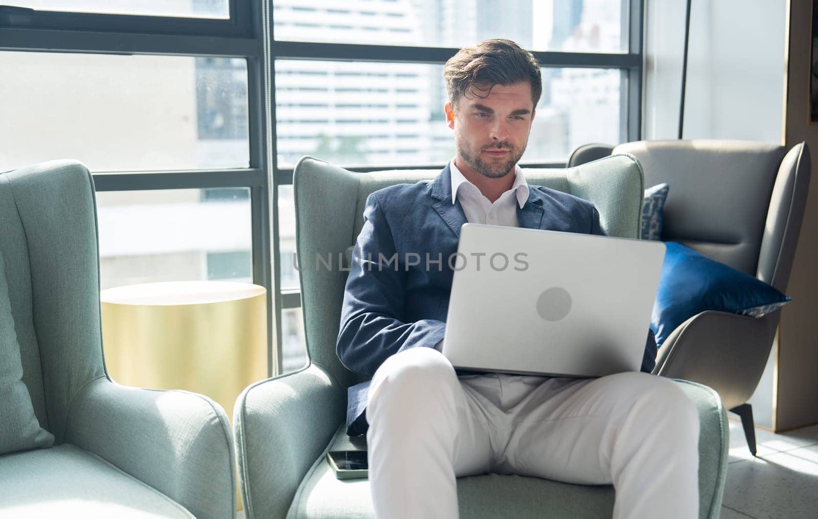 Smart Caucasian business man use labtop to work with sitting on sofa in area of his office and he also look relax and happiness for work.