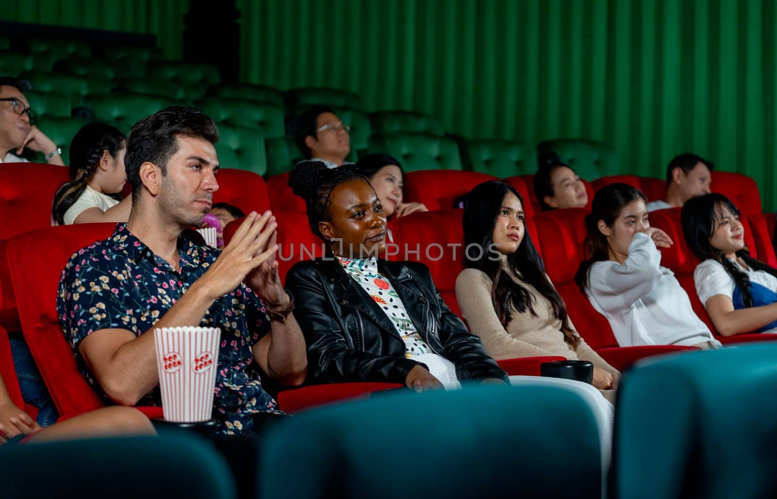 Group of multiethic people sit on seats in cinema theater and they look boring during watch movie and someone sleep in the hall.