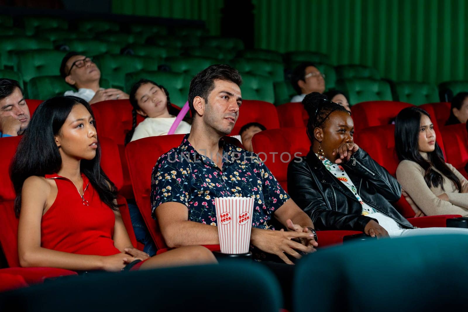 Group of multiethic people sit on seats in cinema theater and they look boring during watch movie and someone sleep in the hall.