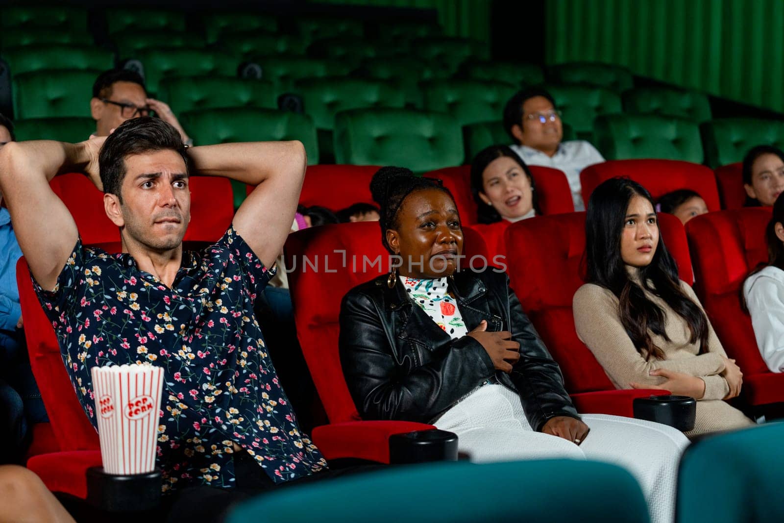 Group of multiethic people sit on seats in cinema theater and they look scary or terify during watch movie.