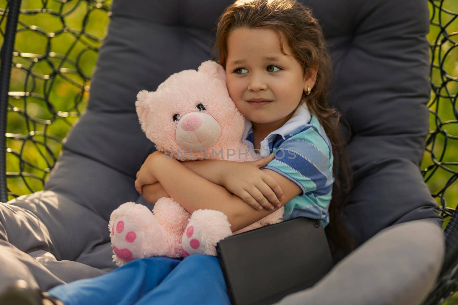 child hugging a teddy bear while sitting in a hanging chair