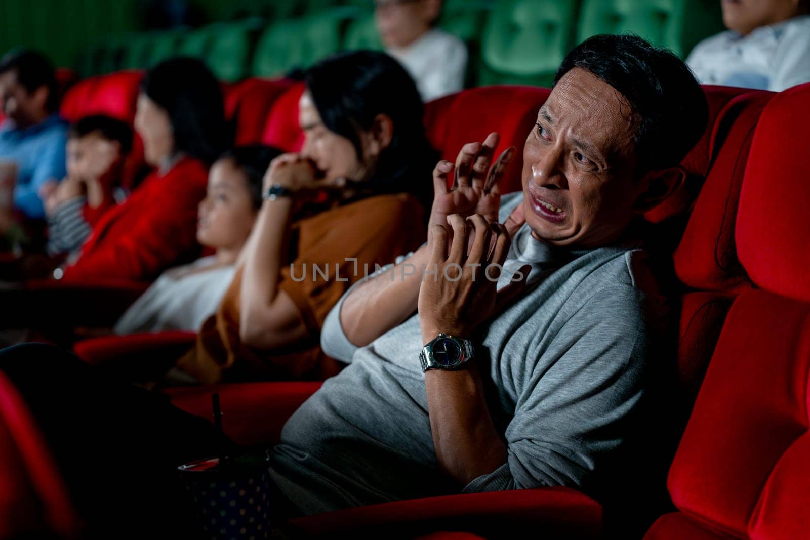 Close up Asian man look scary or panic during watch movie with his family in cinema theater and other people sit beside also express the same action.