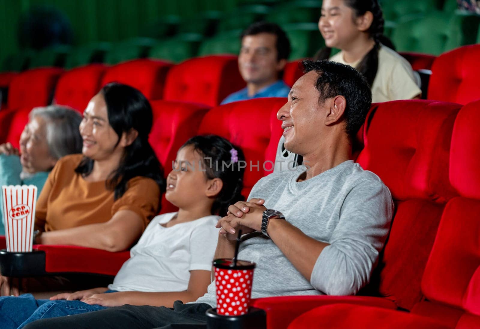 Close up Asian family with father, mother, grandmother and daughter enjoy and happy to watch movie together in cinema theater and they smile in concept of family time for relax on holiday.