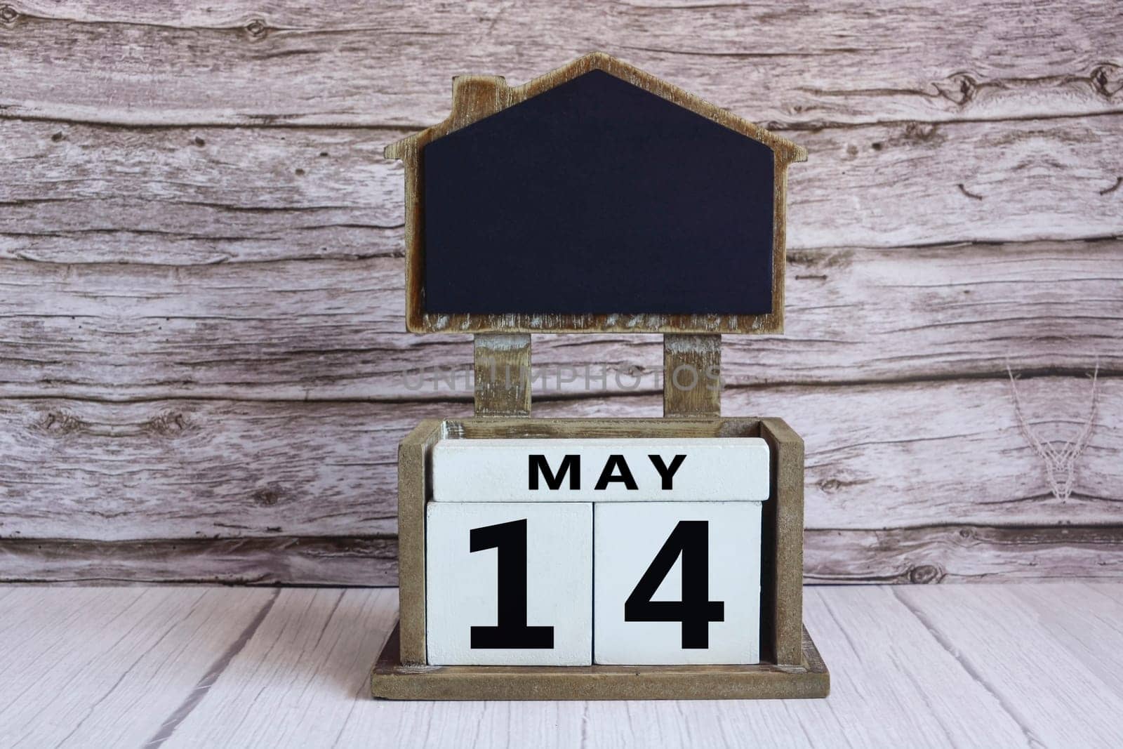 Chalkboard with May 14 calendar date on white cube block on wooden table.