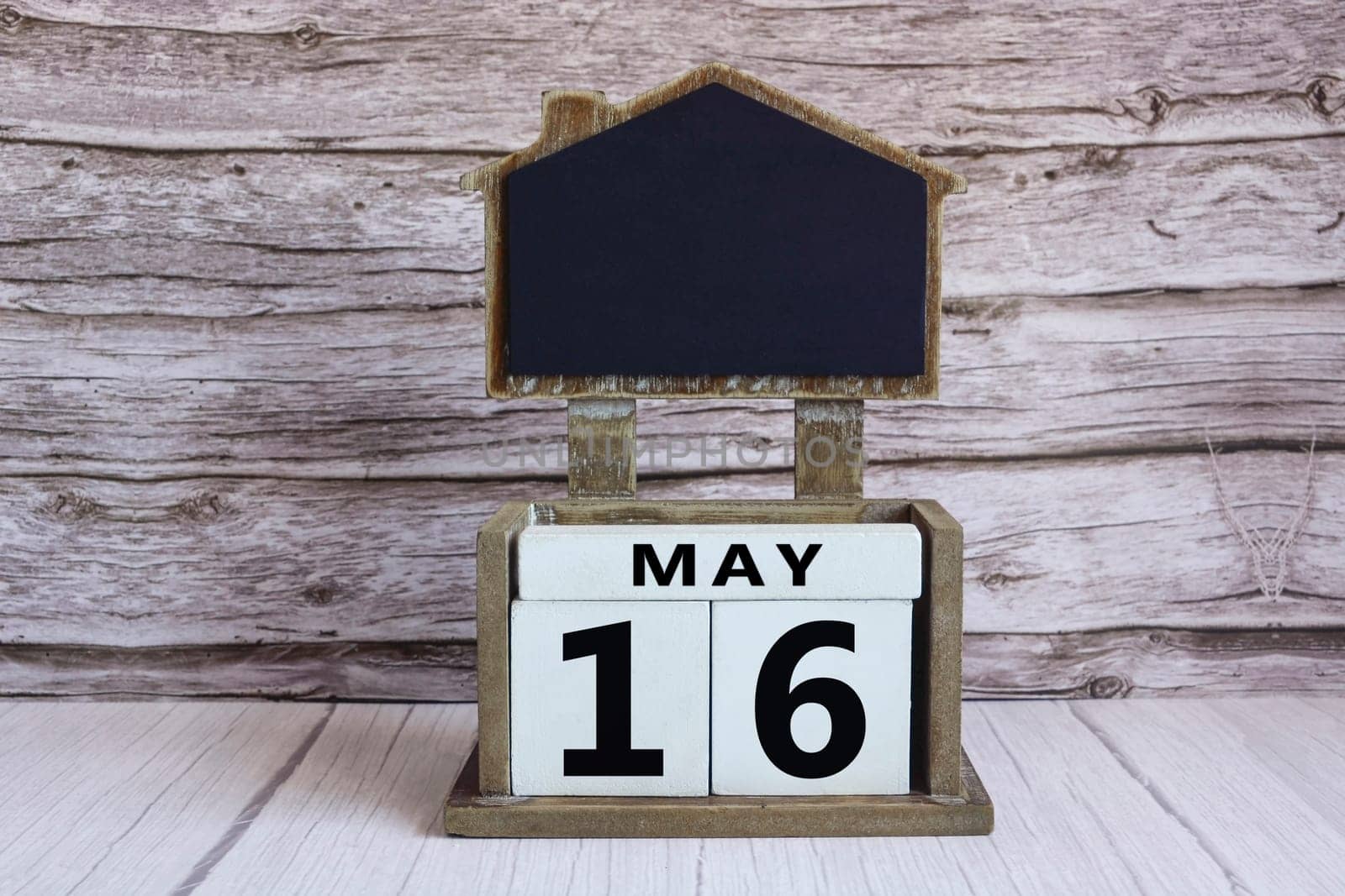 Chalkboard with May 16 calendar date on white cube block on wooden table.