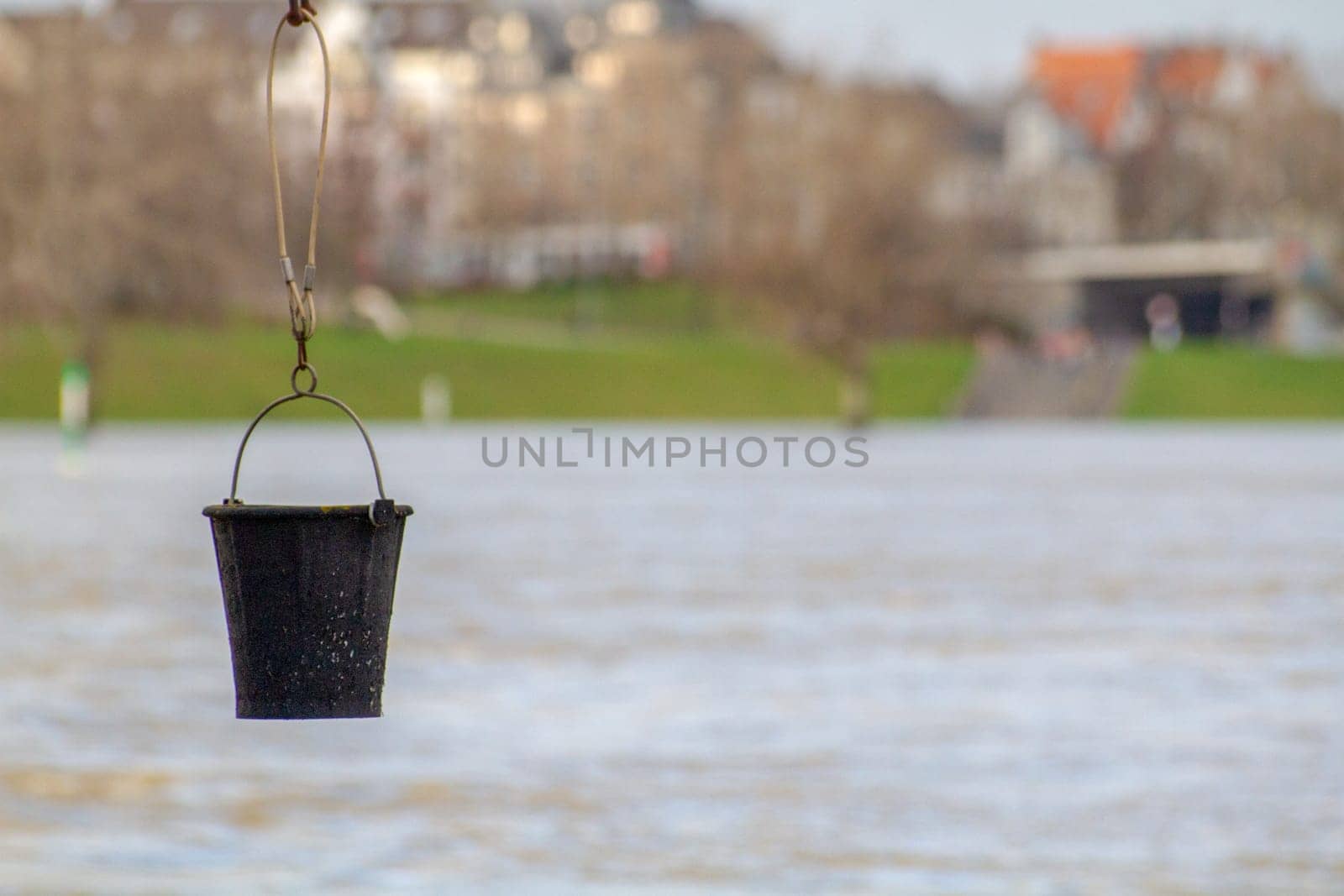 A black bucket hangs against the background of the river by Maksym