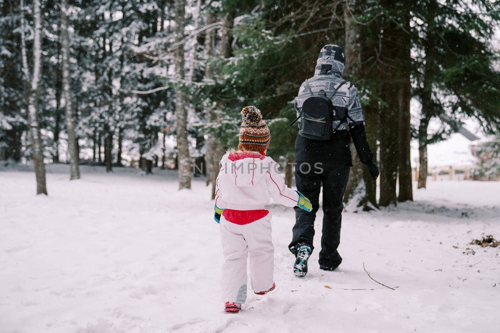 Little girl follows her mother through snowdrifts in a snowy forest. Back view by Nadtochiy