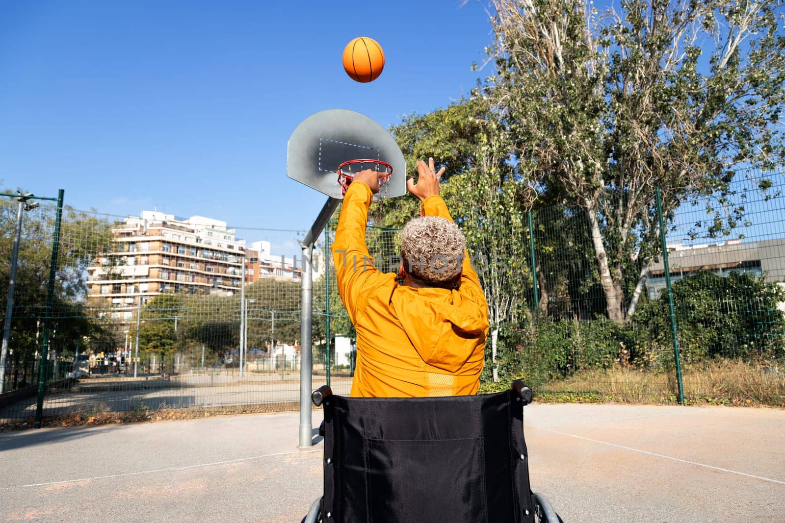 Rear view of African American man in a wheelchair throwing basketball in court playing alone. by Hoverstock