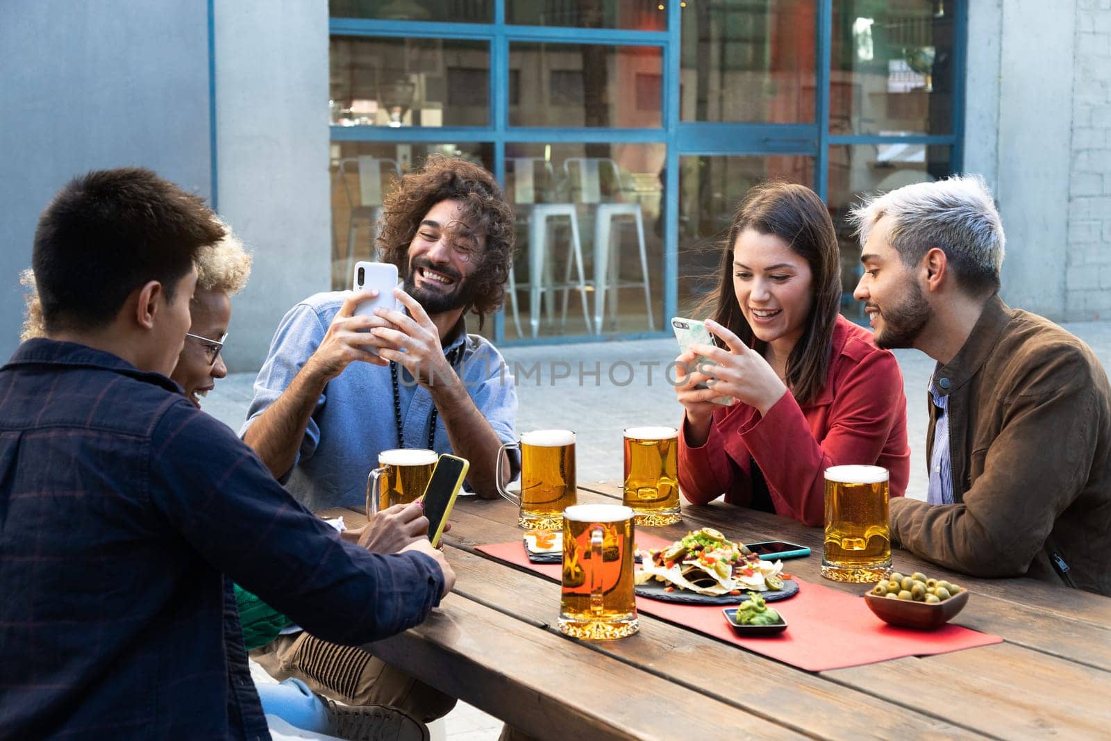 Group of multiracial friends using mobile phones, taking photos and using social media in a bar. Social media addiction concept.