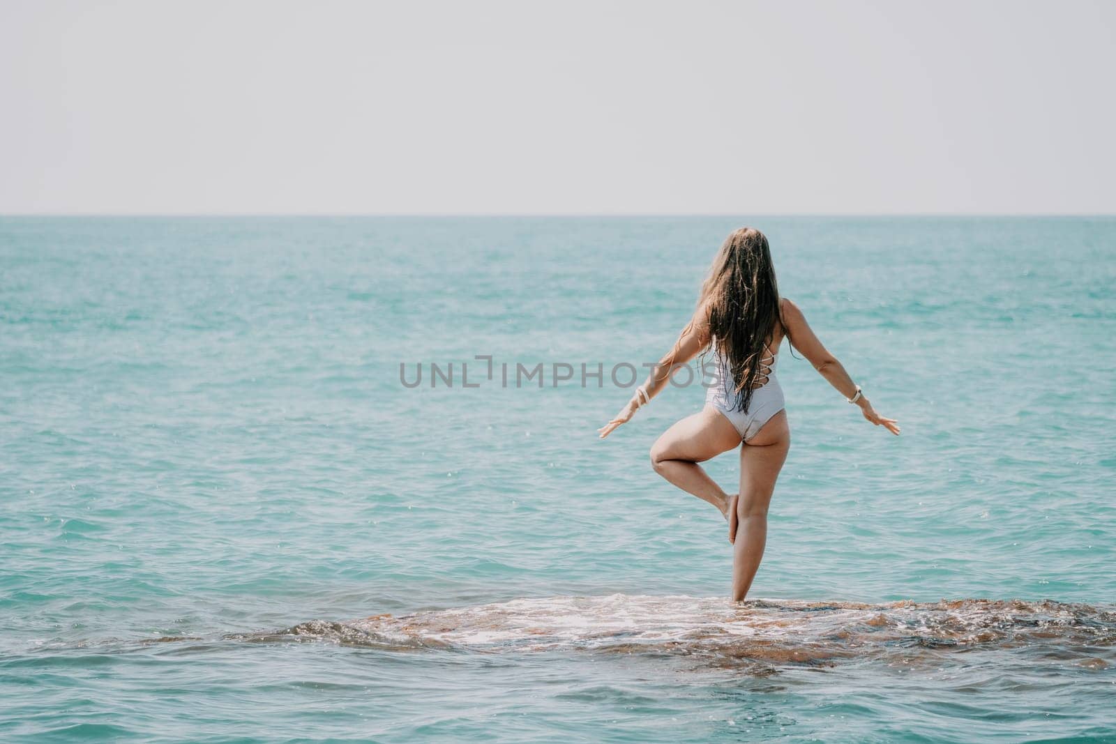 Woman sea yoga. Back view of free calm happy satisfied woman with long hair standing on top rock with yoga position against of sky by the sea. Healthy lifestyle outdoors in nature, fitness concept by panophotograph