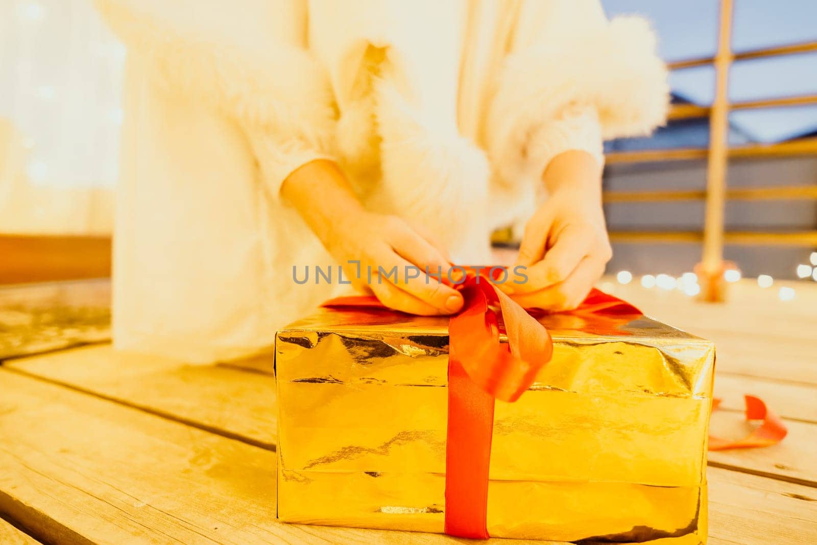 A woman in a white dress is holding a gold box with a red ribbon. She is wearing a crown on her head. The scene takes place in a room with a door and a window. The woman appears to be opening the gift box.