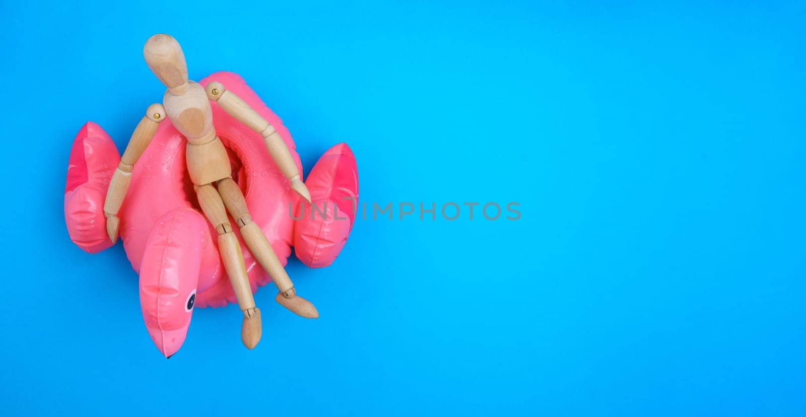 Wooden man relaxing on a pink inflatable swimming circle. Summer vacation at the sea blue background. Copy space, banner