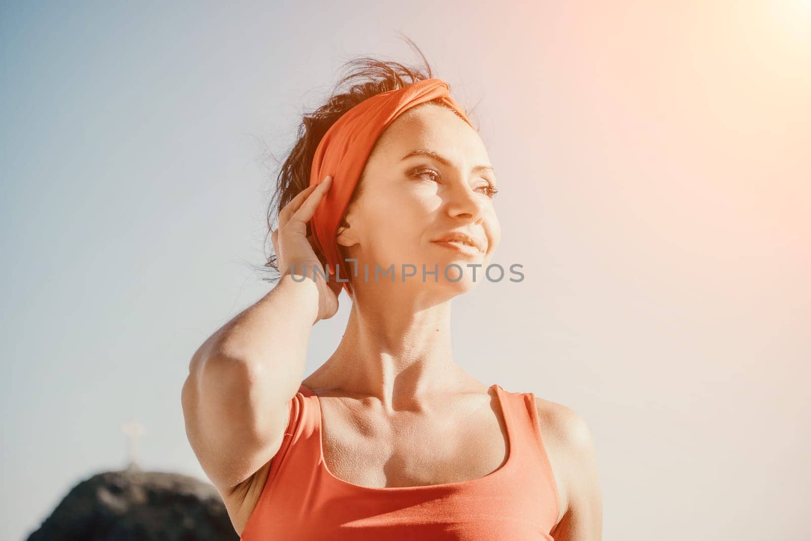 The woman in a red suit practicing yoga on stone at sunrise near the sea. Young beautiful girl in a red bathing suit sits on the seashore in lotus position. Yoga. Healthy lifestyle. Meditation