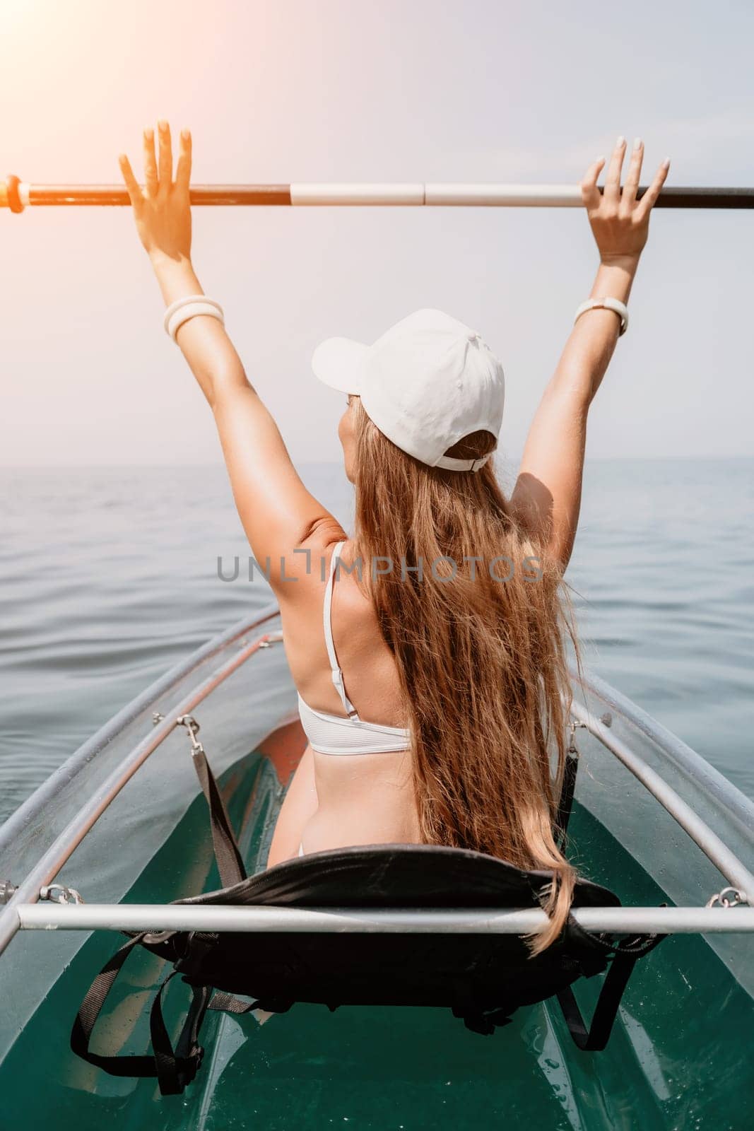 Woman in kayak back view. Happy young woman with long hair floating in transparent kayak on the crystal clear sea. Summer holiday vacation and cheerful female people relaxing having fun on the boat by panophotograph