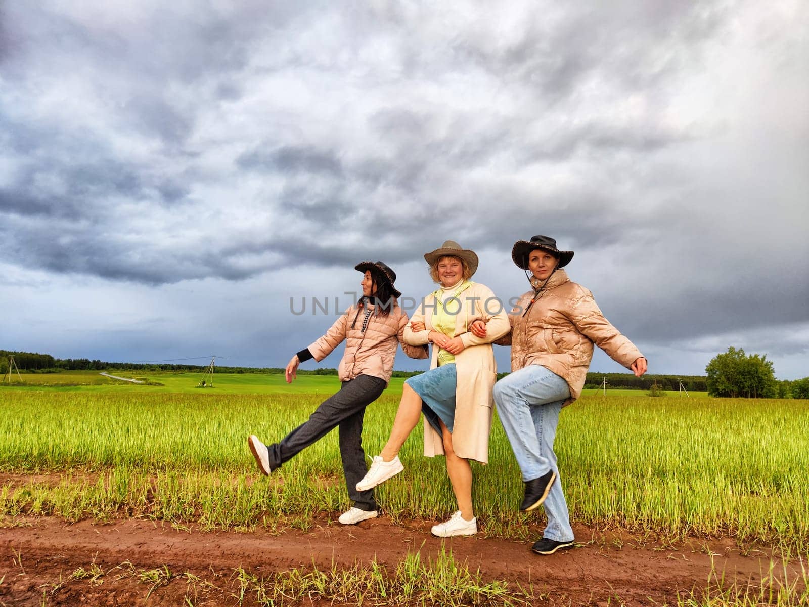 Adult girls looking like a cowboys in hats in a field and with a stormy sky with clouds posing in the rain. Women having fun outdoors on rural and rustic nature