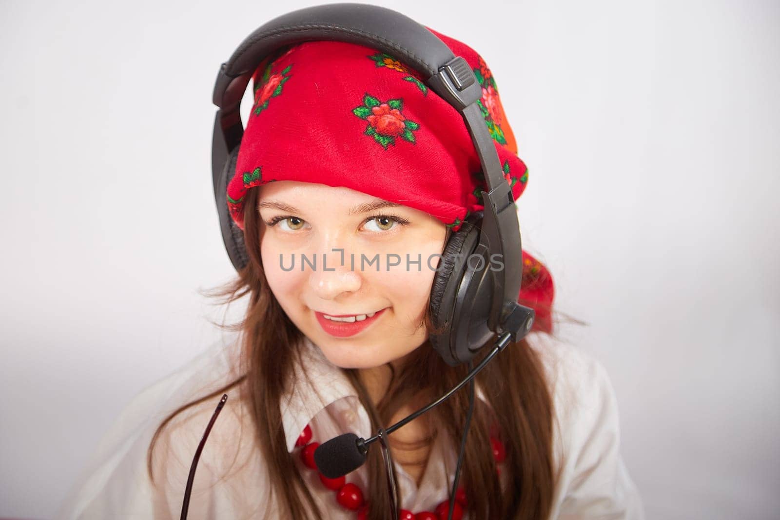 Portrait of young girl in red scarf, large headphones with microphone and black glasses. Woman who is radio or television presenter in the workplace. Funny female telecom operator. Freelancer at work by keleny