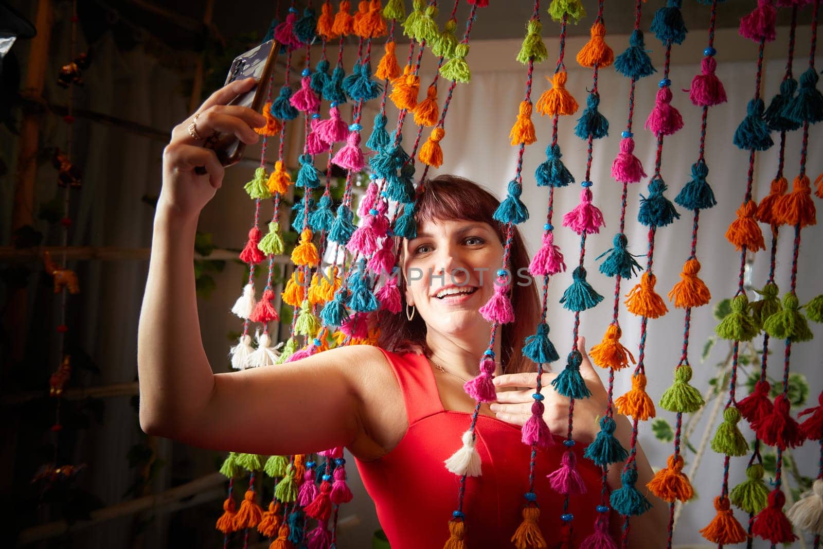 Funny, cute, self-confident adult girl posing in a red dress and taking a selfie. A middle-aged model at a photo shoot in studio for social networks. Leisure activities