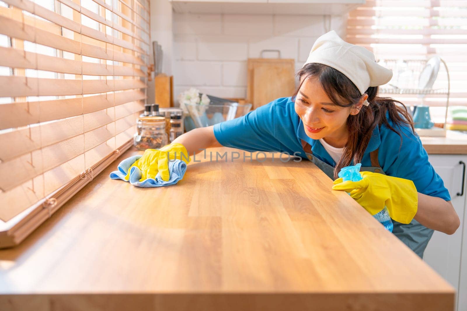 Asian housekeeper smile with happiness use towel to clean area in kitchen with day light and she look enjoy to work in customer house.