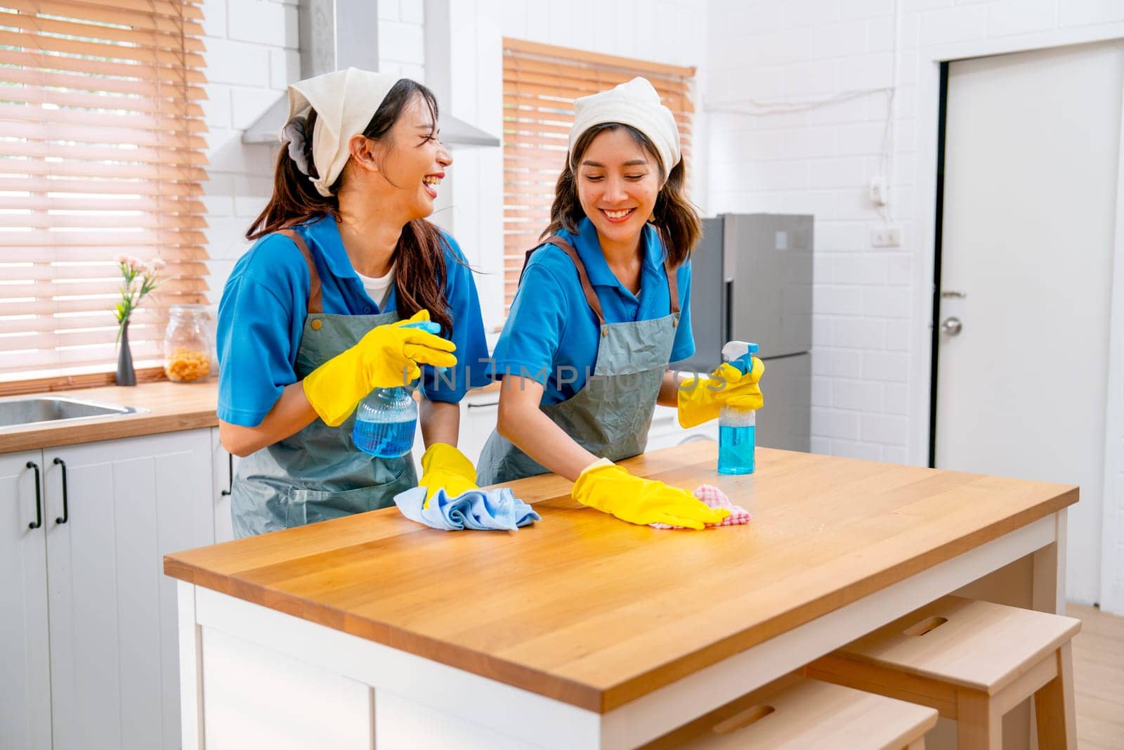 Two Asian housekeeper or housemaid women enjoy to work and teasing each other during clean table in kitchen at customer house.