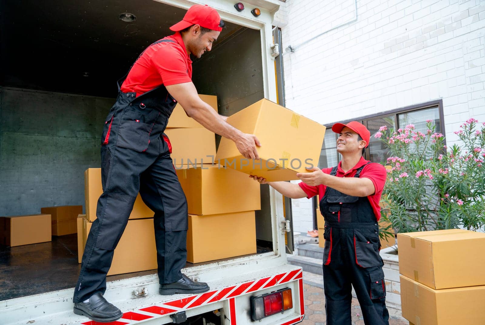 Close up of delivery man stand on truck and send parcel or box to his co-worker during transport the product to customer house. by nrradmin