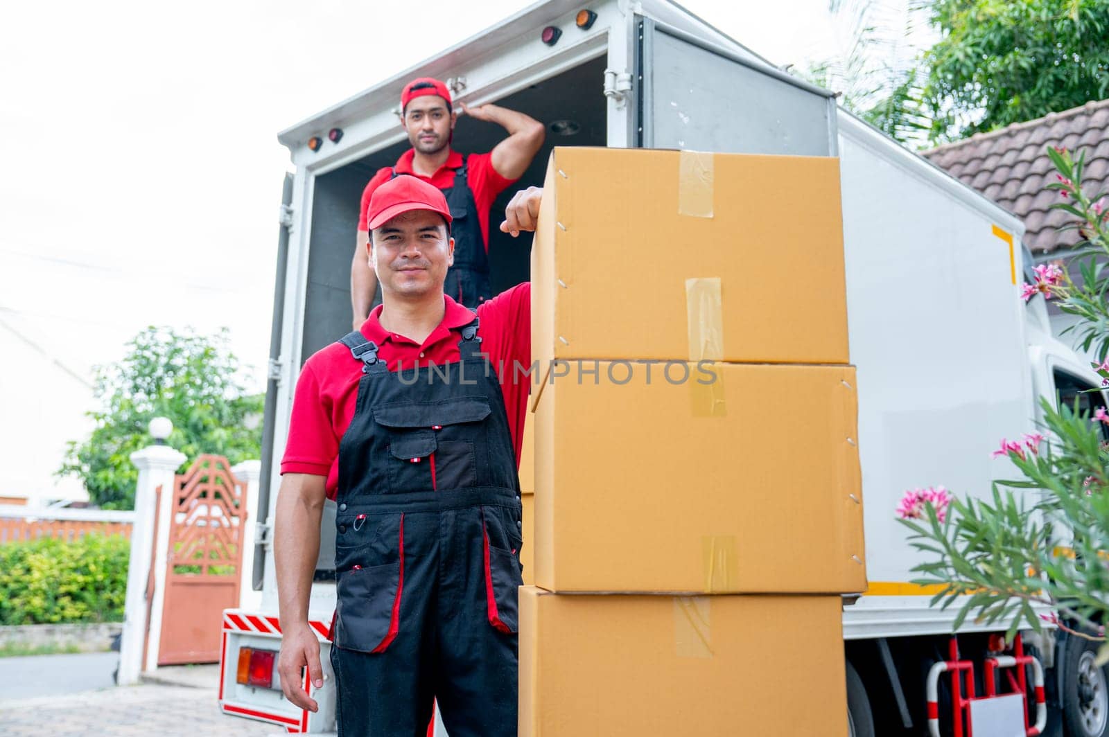 Portrait of delivery man stand near stack of boxes and look at camera with smiling and his co-worker stand in the back on truck. by nrradmin