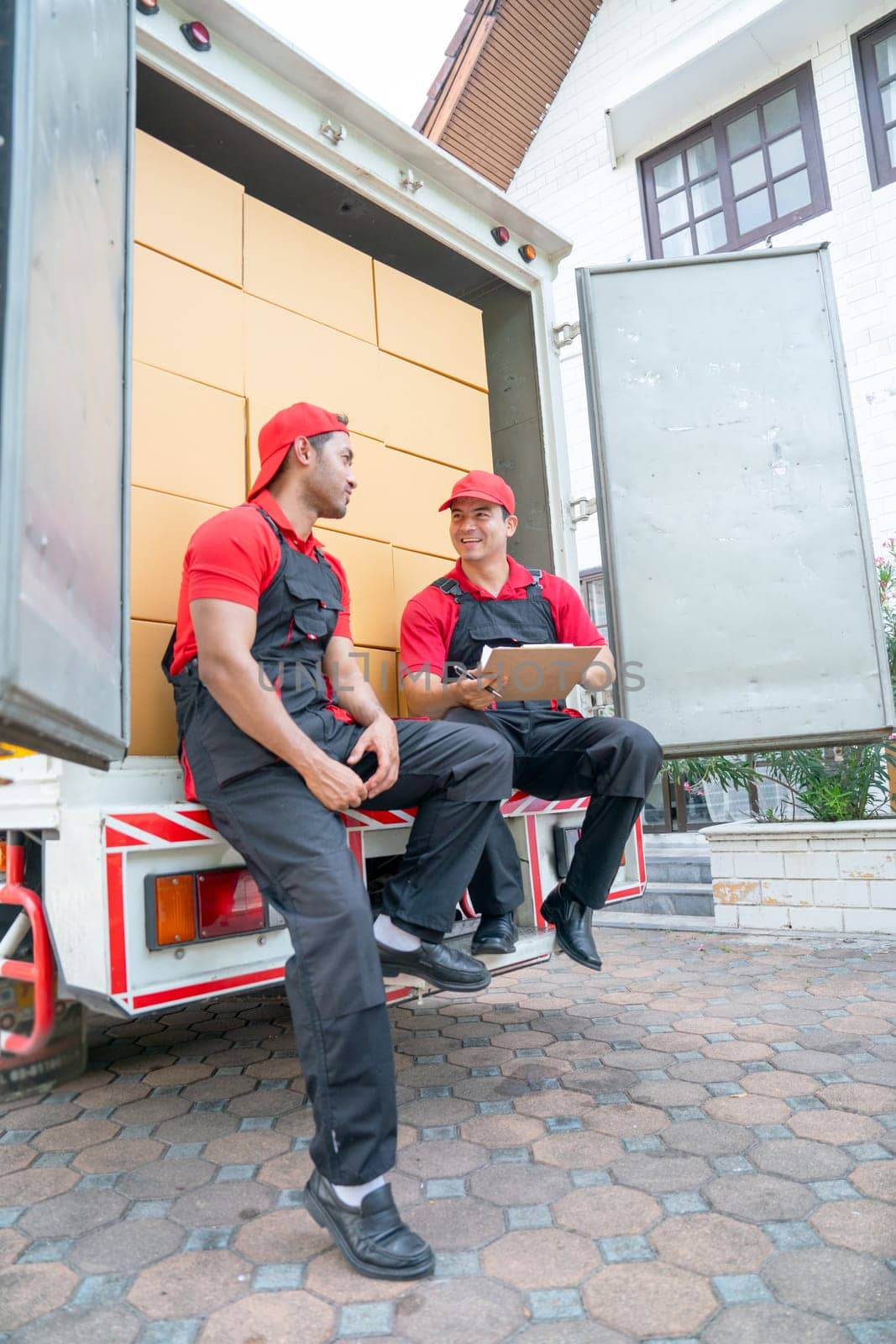 Vertical image of two delivery men sit and discuss together on back part of truck during move package or boxes to customer house.