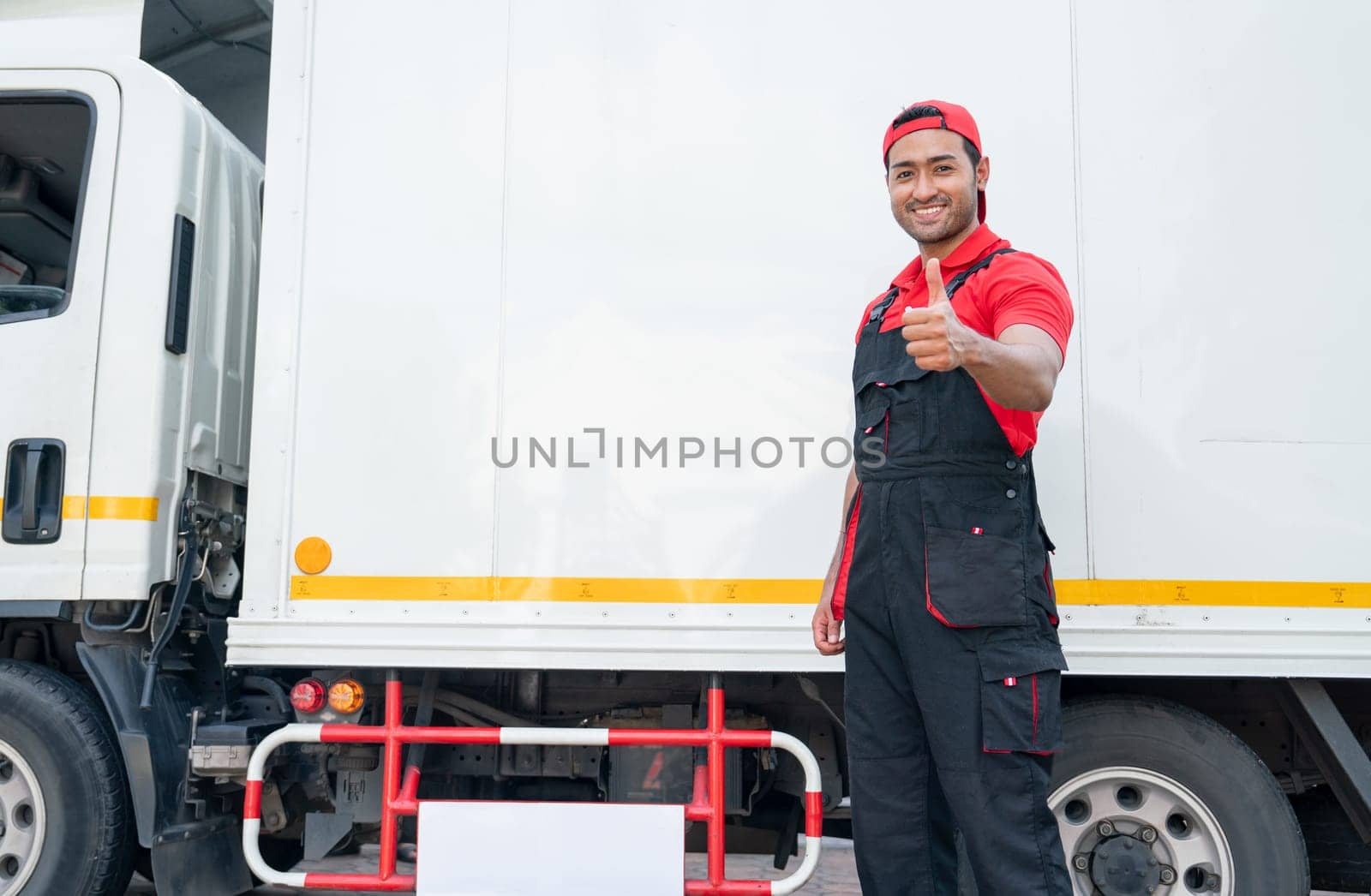 Portrait of Asian delivery man stand beside of truck and show thumbs up also look at camera with smiling after finish to send the product to customer house. by nrradmin