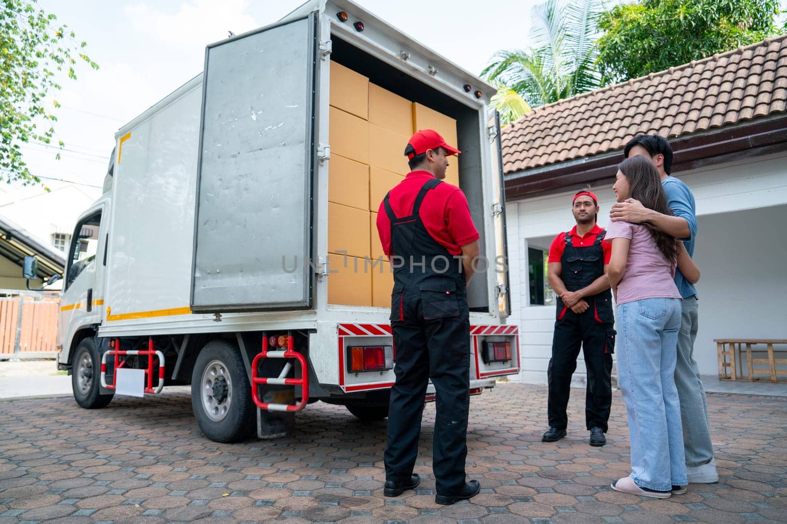 Wide shot of two delivery man opern truck door and show to couple people as customer at the house and they look happy. by nrradmin