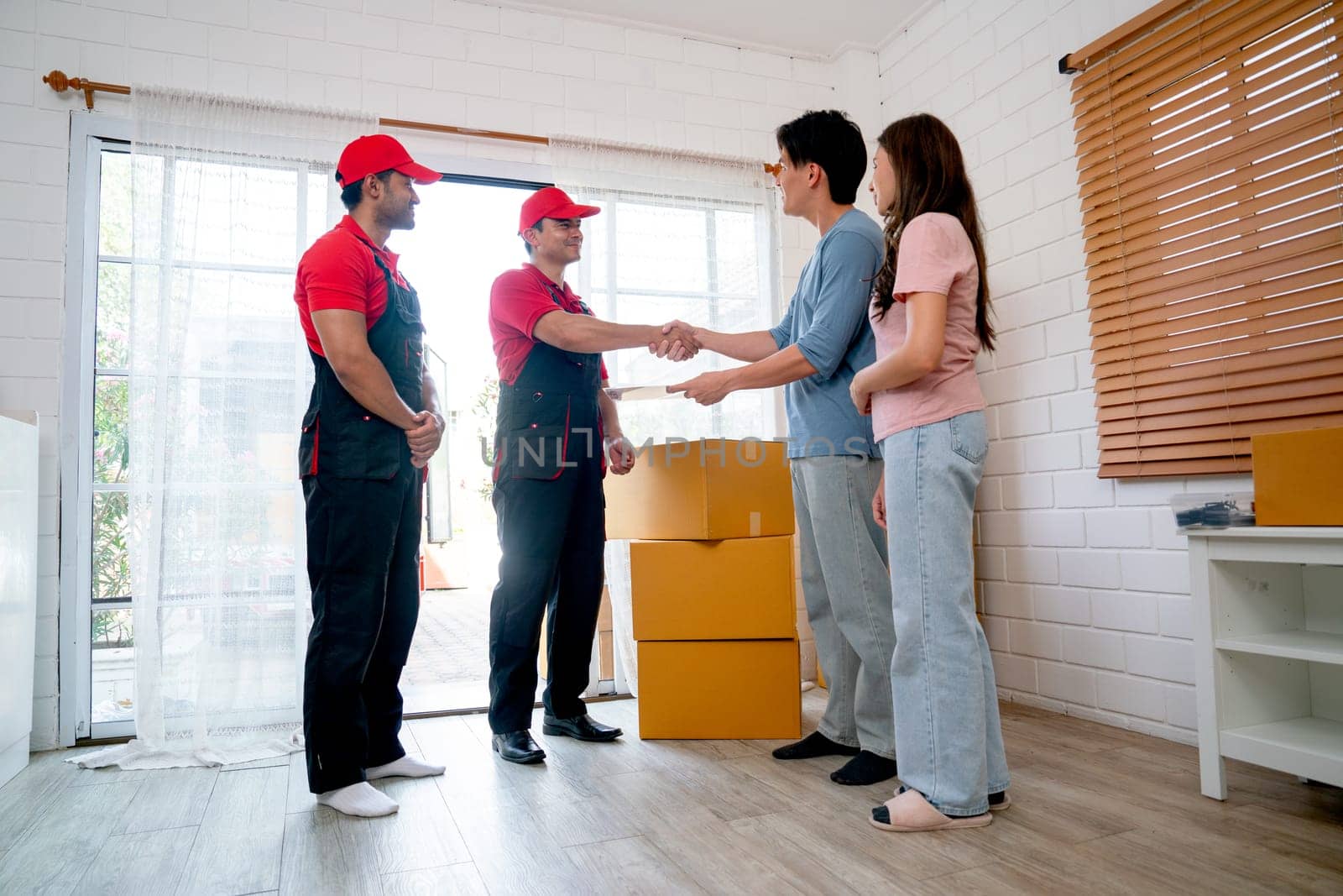 Asian man stand with his wife also shake hands to delivery men during process to send product to customer house. by nrradmin