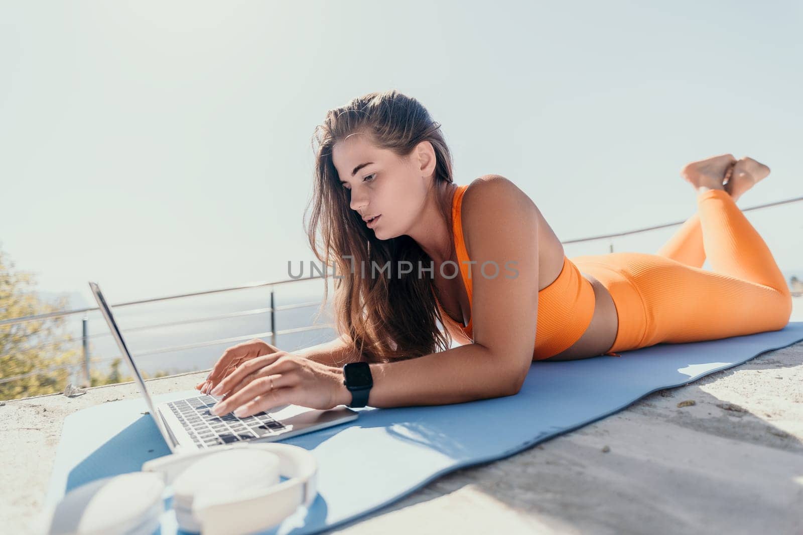 Digital nomad, Business woman working on laptop by the sea. Pretty lady typing on computer by the sea at sunset, makes a business transaction online from a distance. Freelance, remote work on vacation