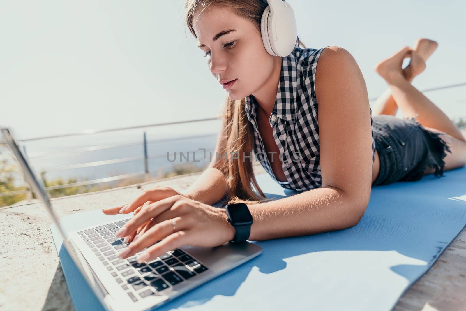 Woman laptop sea. Working remotely on seashore. Happy successful woman female freelancer working on laptop by the sea at sunset, makes a business transaction online. Freelance, remote work on vacation by panophotograph