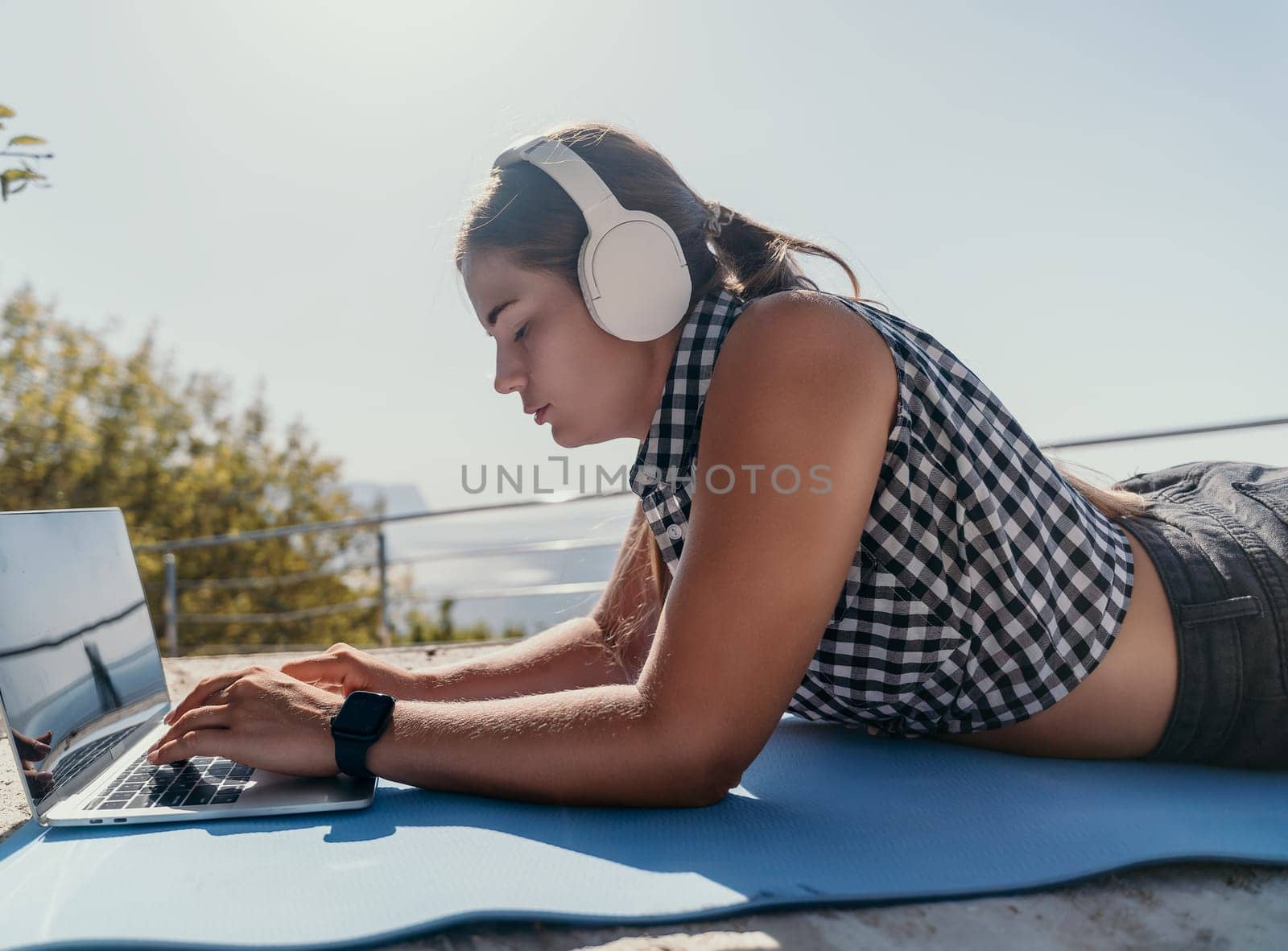 Woman laptop sea. Working remotely on seashore. Happy successful woman female freelancer working on laptop by the sea at sunset, makes a business transaction online. Freelance, remote work on vacation by panophotograph