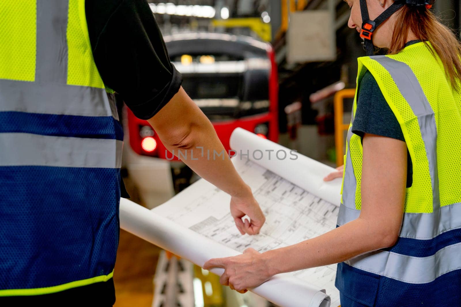 Close up hands of engineer or technician worker point to drawing paper and discuss with co-worker woman and they stay in front of electric train in factory workplace or maintenance center.