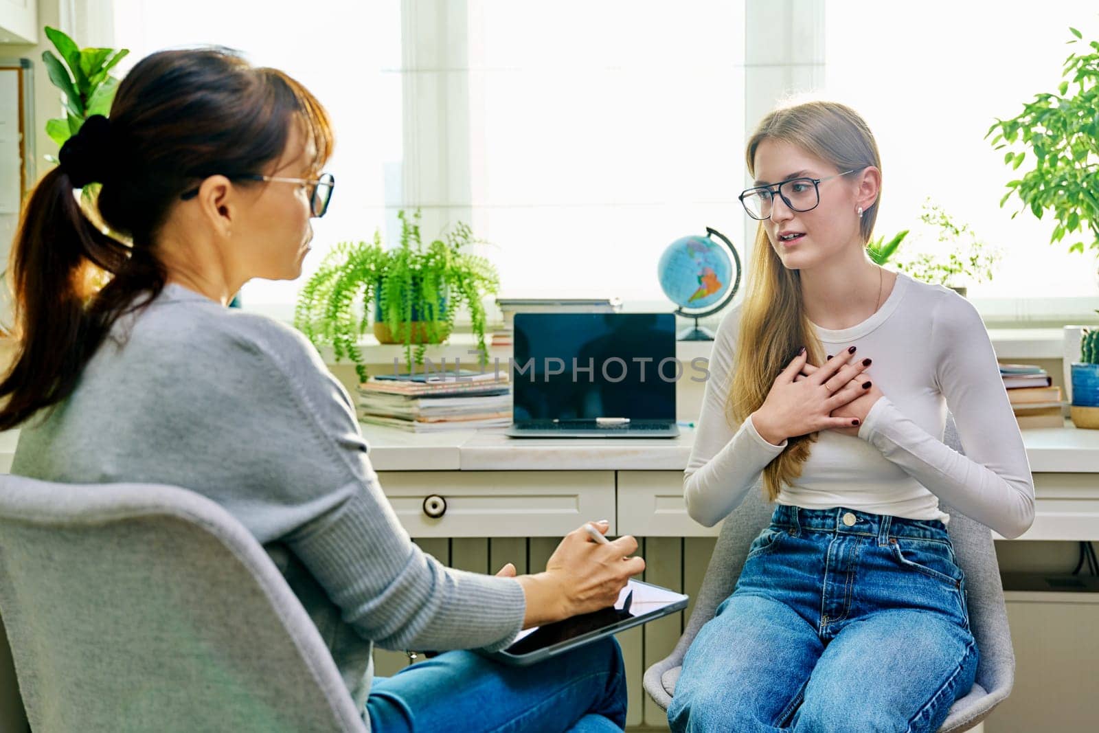 Young female teenager 16, 17 years old talking with counselor psychologist behavior social worker teacher, sitting in chair in office. Psychology psychotherapy therapy mental health adolescence youth