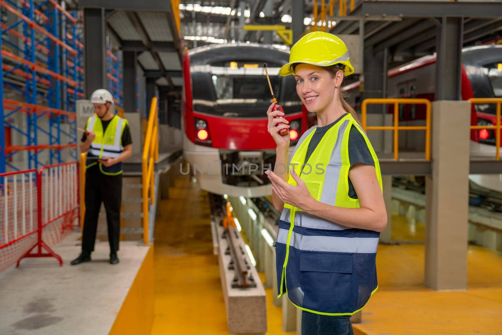 Professional engineer or technician worker woman hold walkie talkie and look at camera also stay in front of electric train in factory workplace or maintenance center.