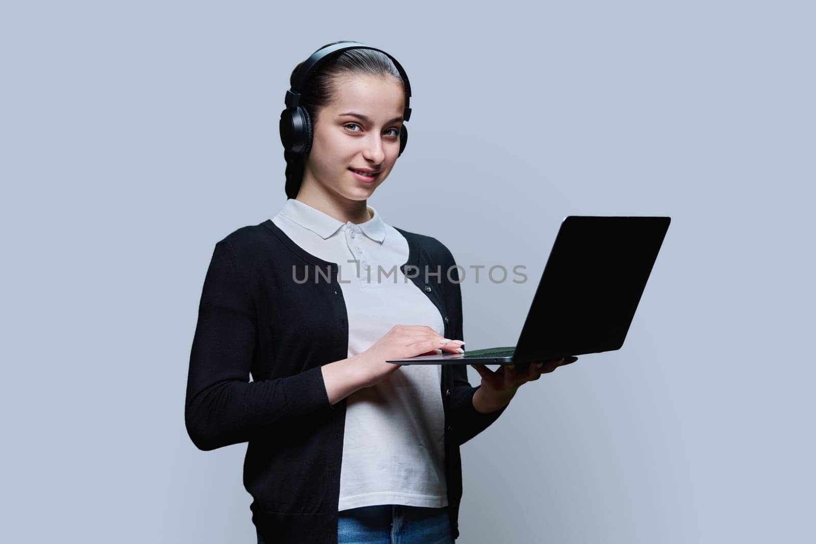 Teen girl student wearing headphones using laptop, on grey background by VH-studio