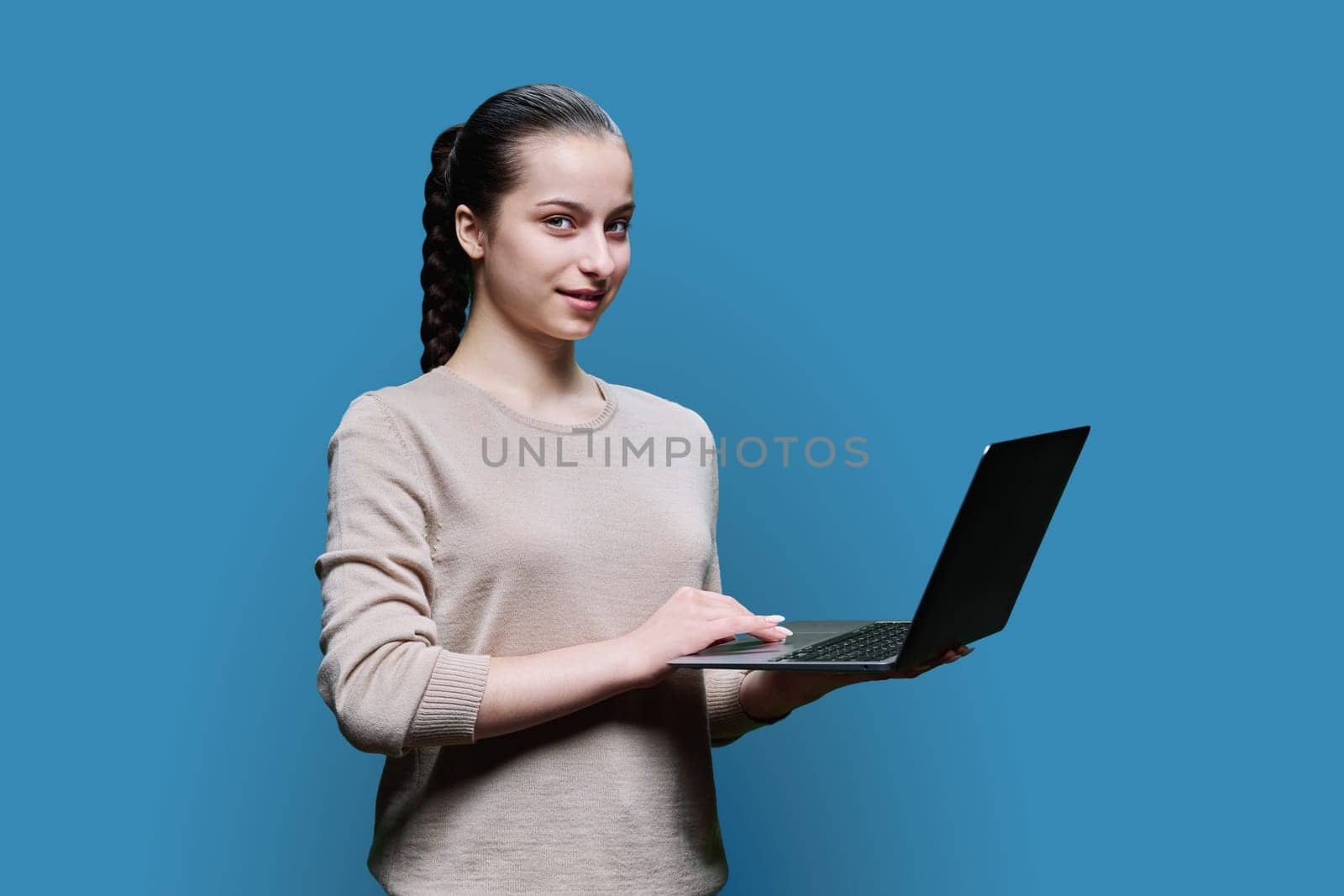 Teen girl high school student using laptop looking at camera on blue background by VH-studio