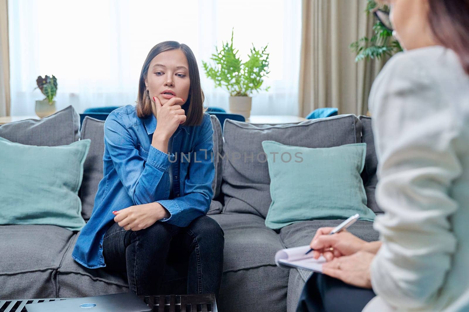 Sad young woman at therapy session with psychologist, psychiatrist. Therapist counselor and unhappy female patient on sofa in office. Psychology counseling treatment psychotherapy mental health youth