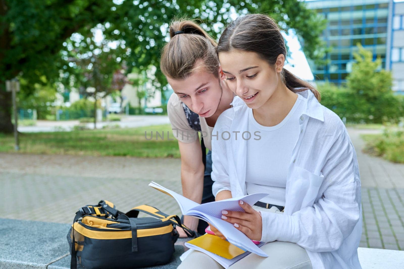 Two high school students guy and girl outdoor, school building background. Education, friendship, youth, adolescence concept