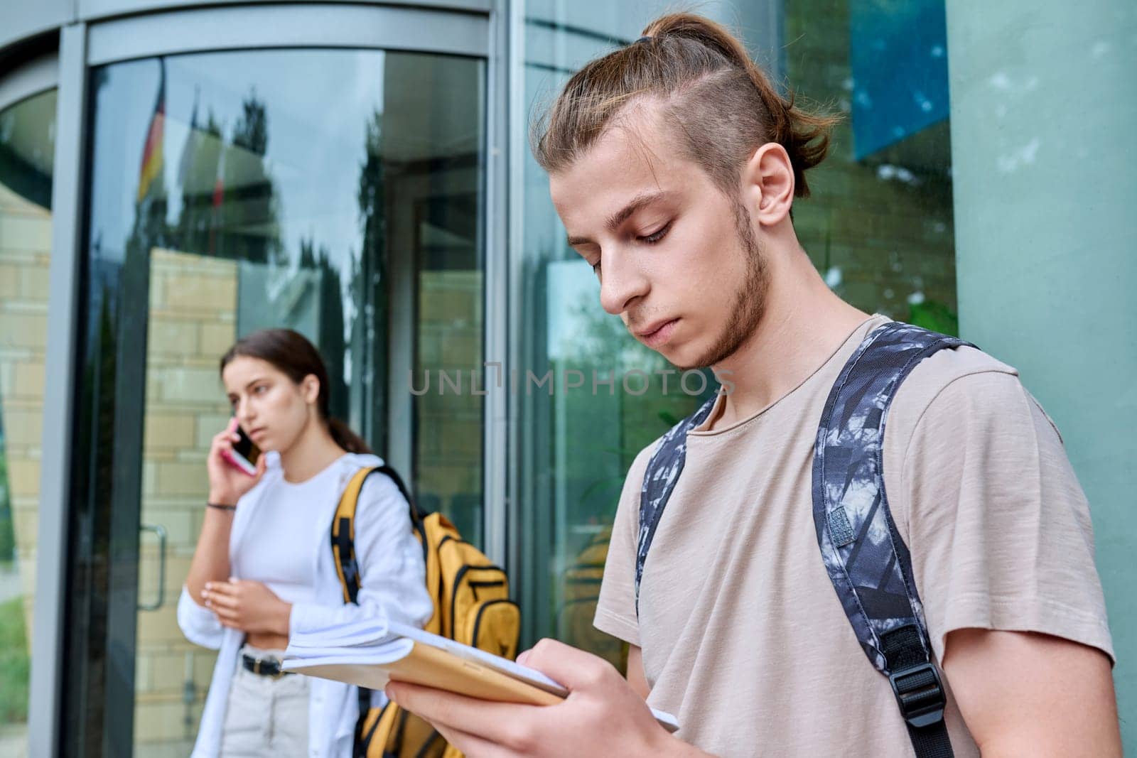 Guy teenager student with backpack notebooks outdoor, educational building background by VH-studio