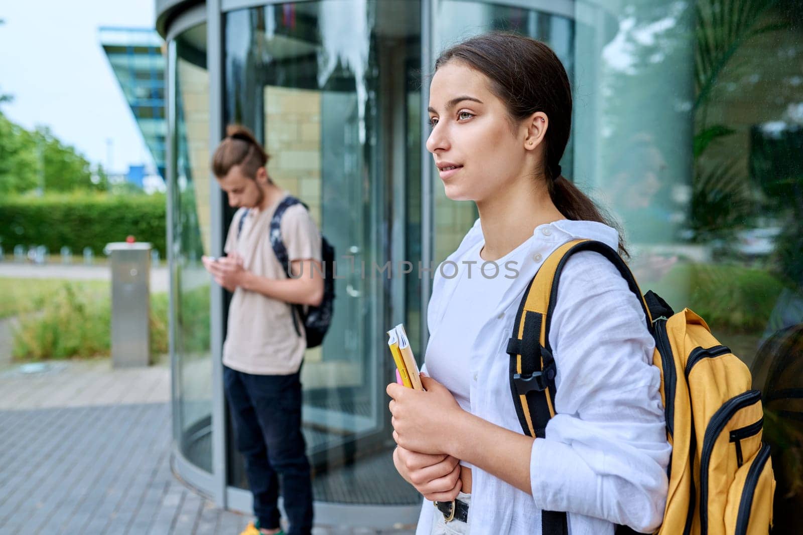 Portrait of high school student, smiling girl with backpack textbooks outdoor, educational building background. Adolescence, 15, 16, 17 years old, lifestyle, education concept