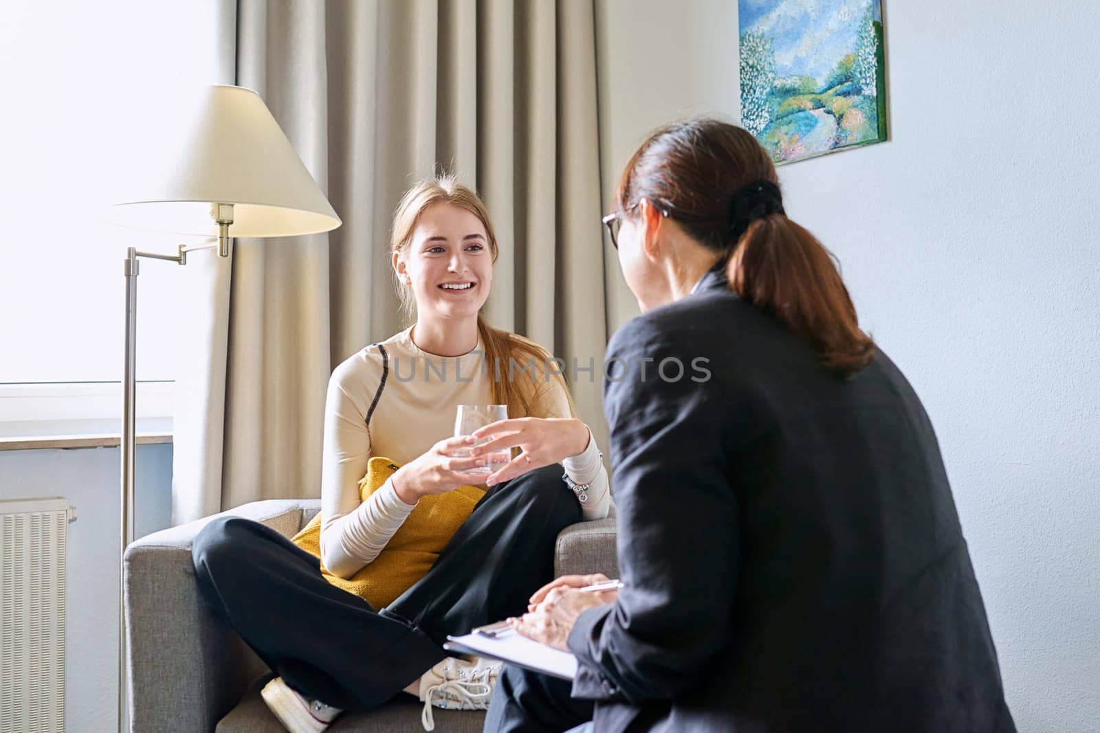 Young female teenager 16, 17 years old talking with counselor psychologist behavior social worker teacher, sitting in chair in office. Psychology psychotherapy therapy mental health adolescence youth