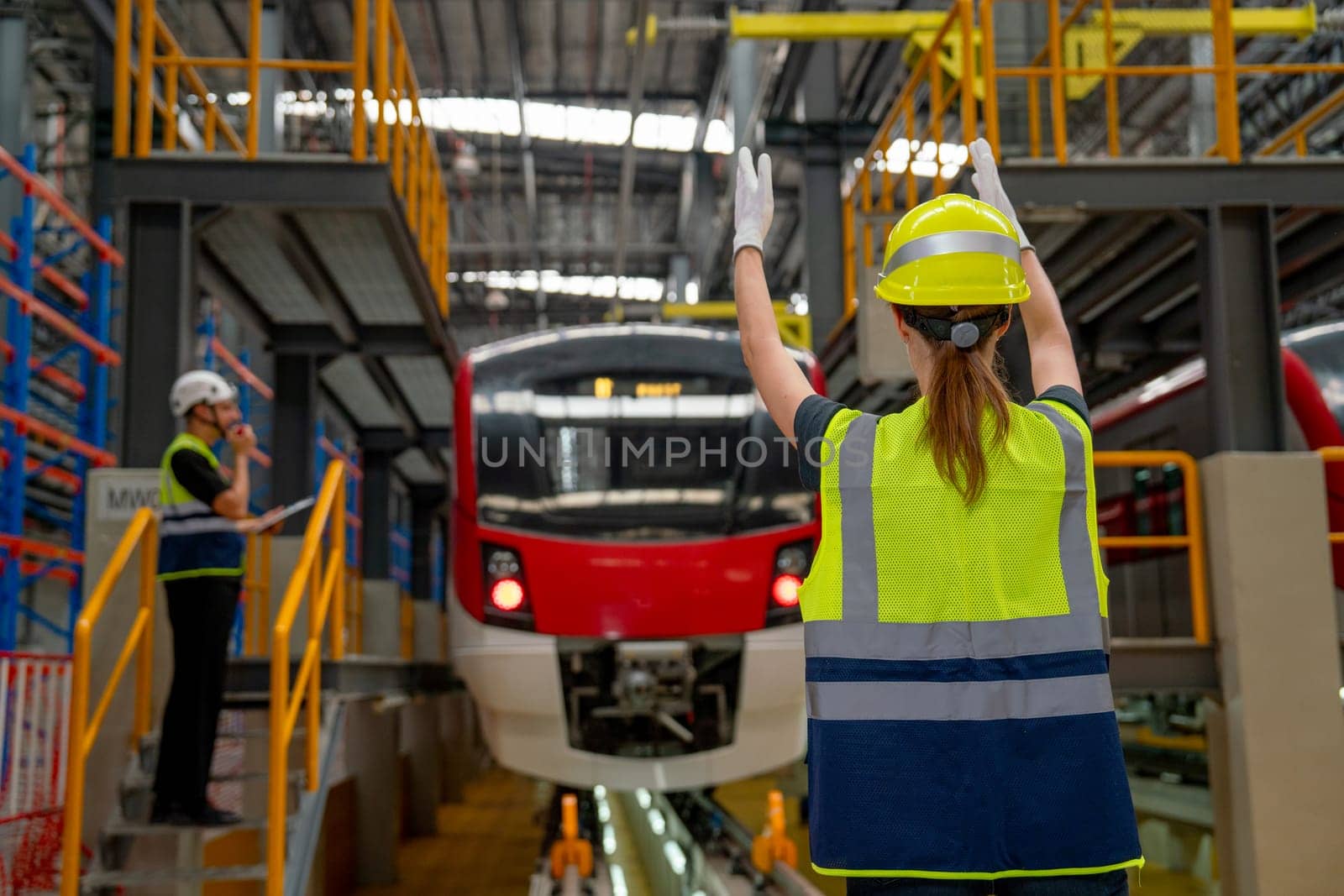 Technician or factory worker woman stand and show action to the driver in electric train in factory workplace and co-worker also stay near the train.