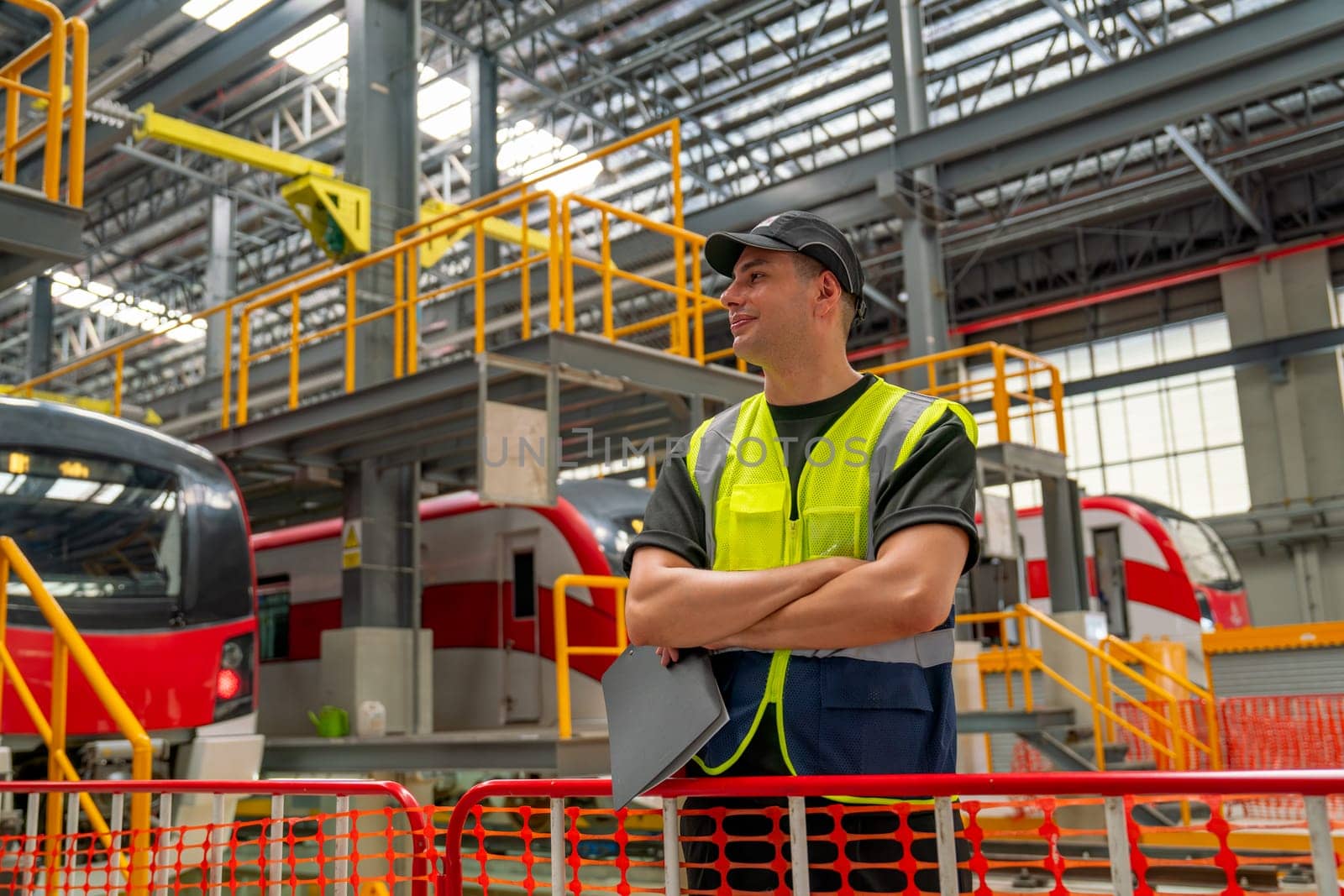 Professional engineer or technician worker man stand with arm-crossed in front of electric train and he look happy to work in factory workplace of maintenance center.