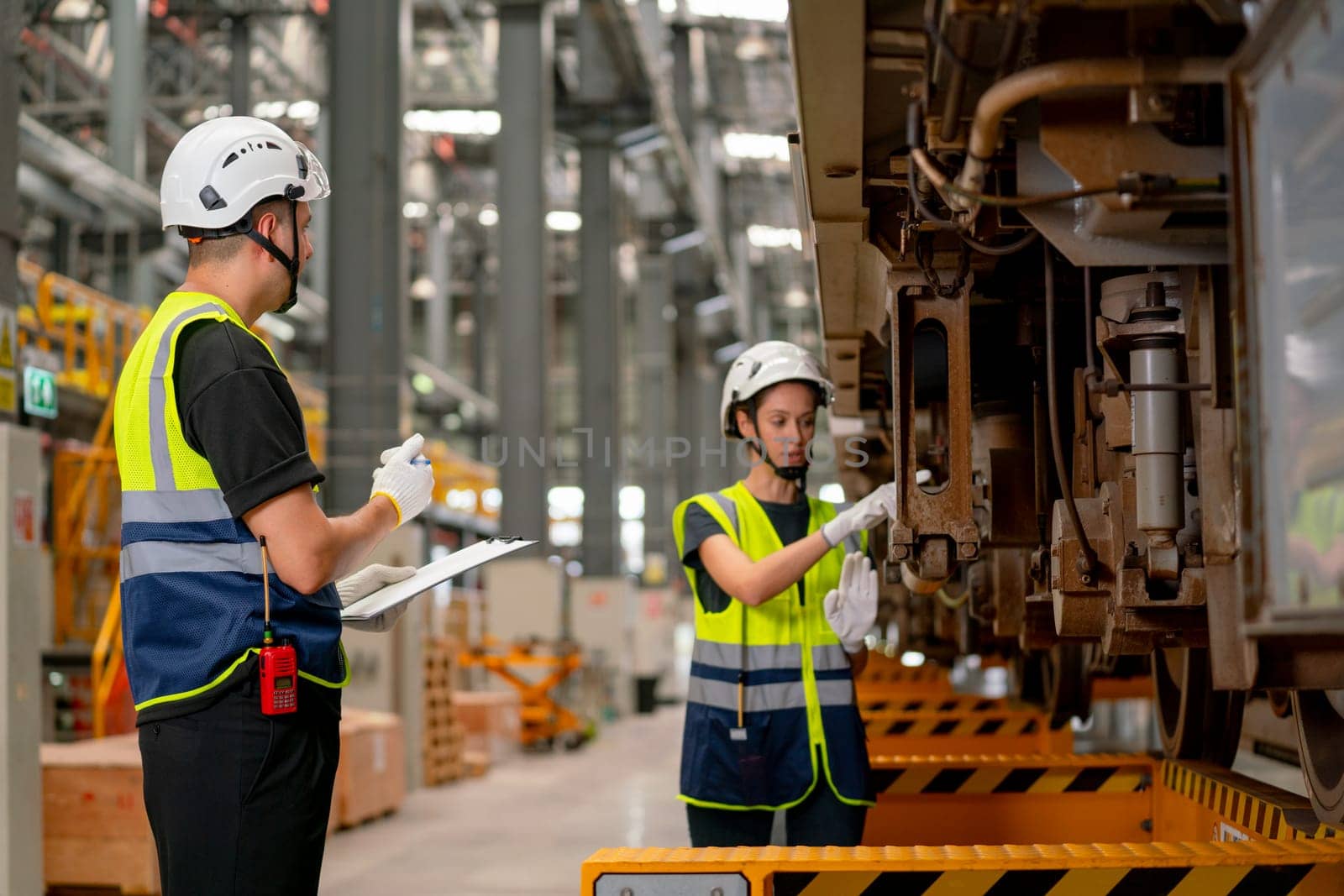 Professional engineer or technician worker woman check and discuss the problem of parts under electric train with co-worker man in workplace area.