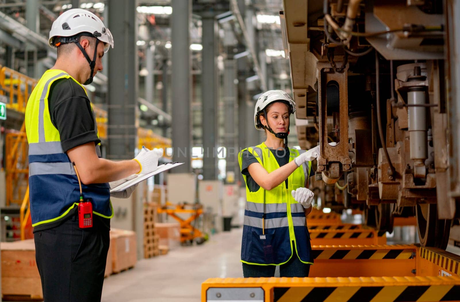 Professional engineer or technician worker woman check and discuss the problem of parts under electric train with co-worker man in workplace area.