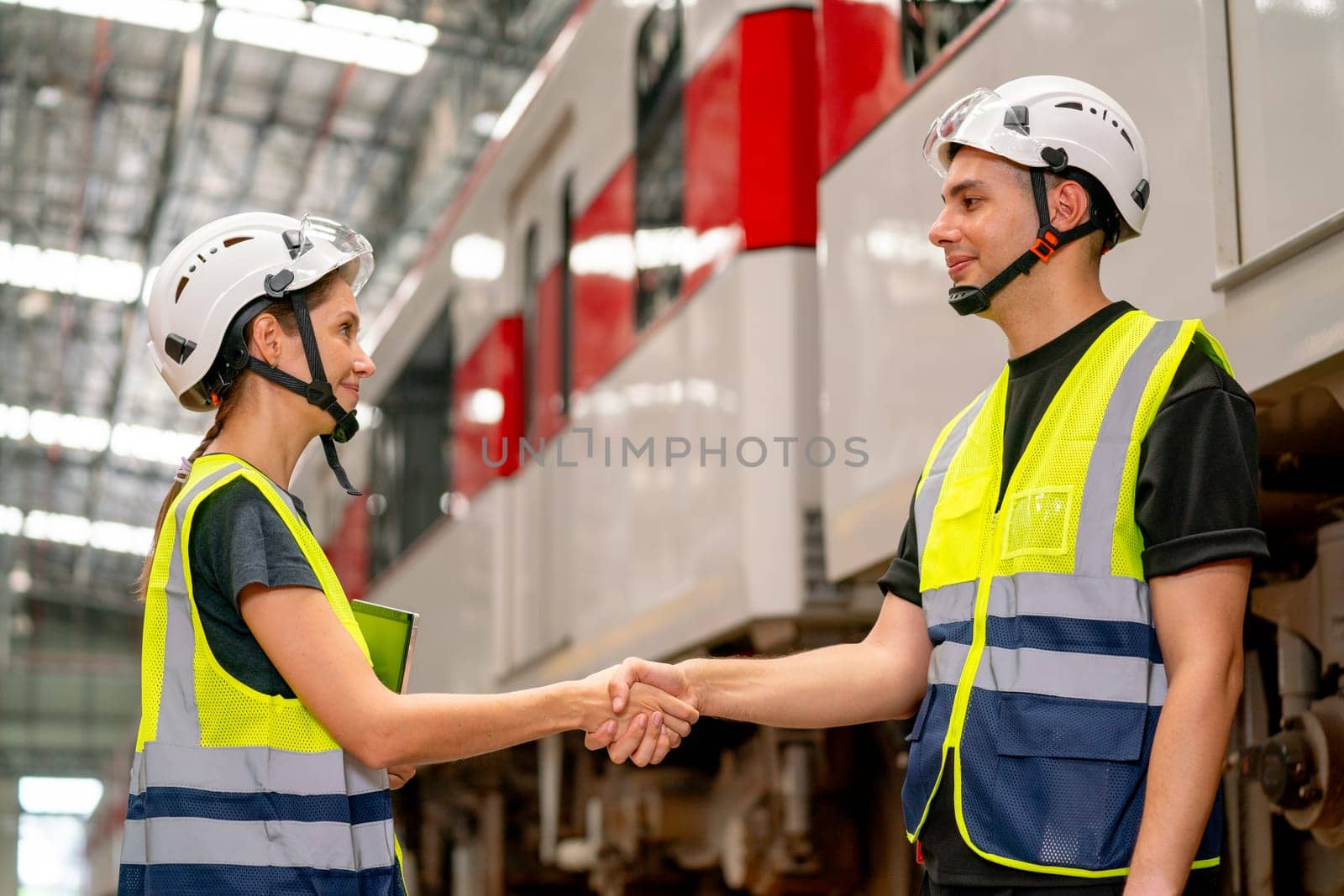 Close up professional engineer or factory technician worker man and woman shake hands for the success of joined project together in workplace near the electric train on rail.