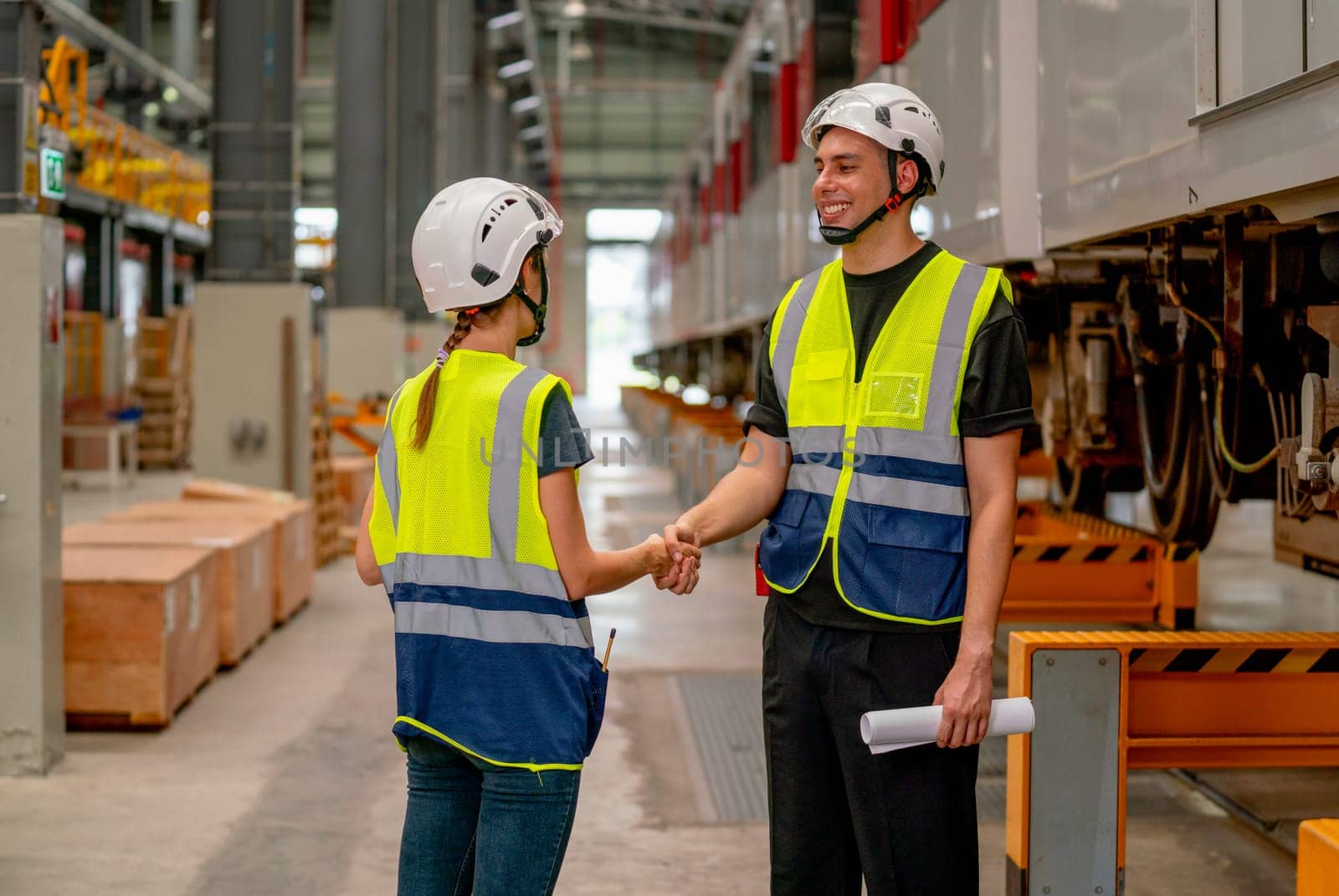 Engineer or factory technician worker man and woman shake hands for the success of joined project together in workplace near the electric train on rail. by nrradmin