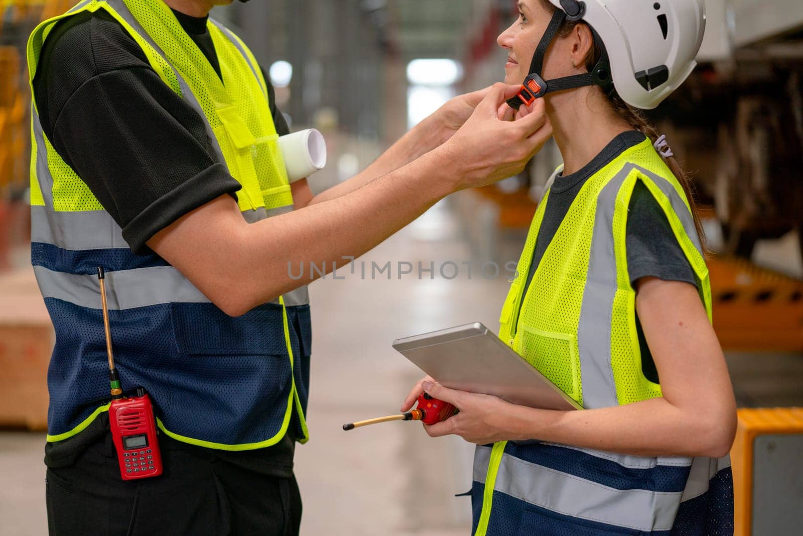 Close up technician man help to set or fix problem of strap of hardhat of engineer or factory worker woman and they stay in factory or workplace area.