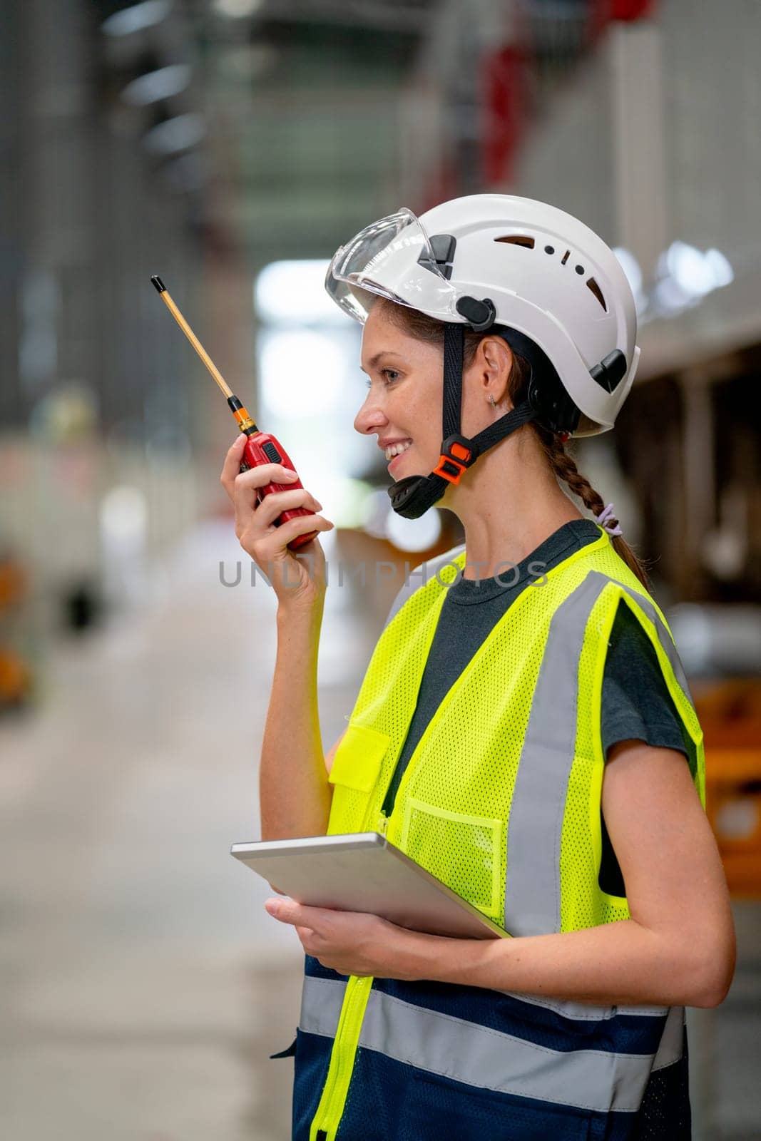 Vertical image of pretty factory worker woman use walkie talkie to contact with team or co-worker and also hold tablet also stay near the train with happiness for work.